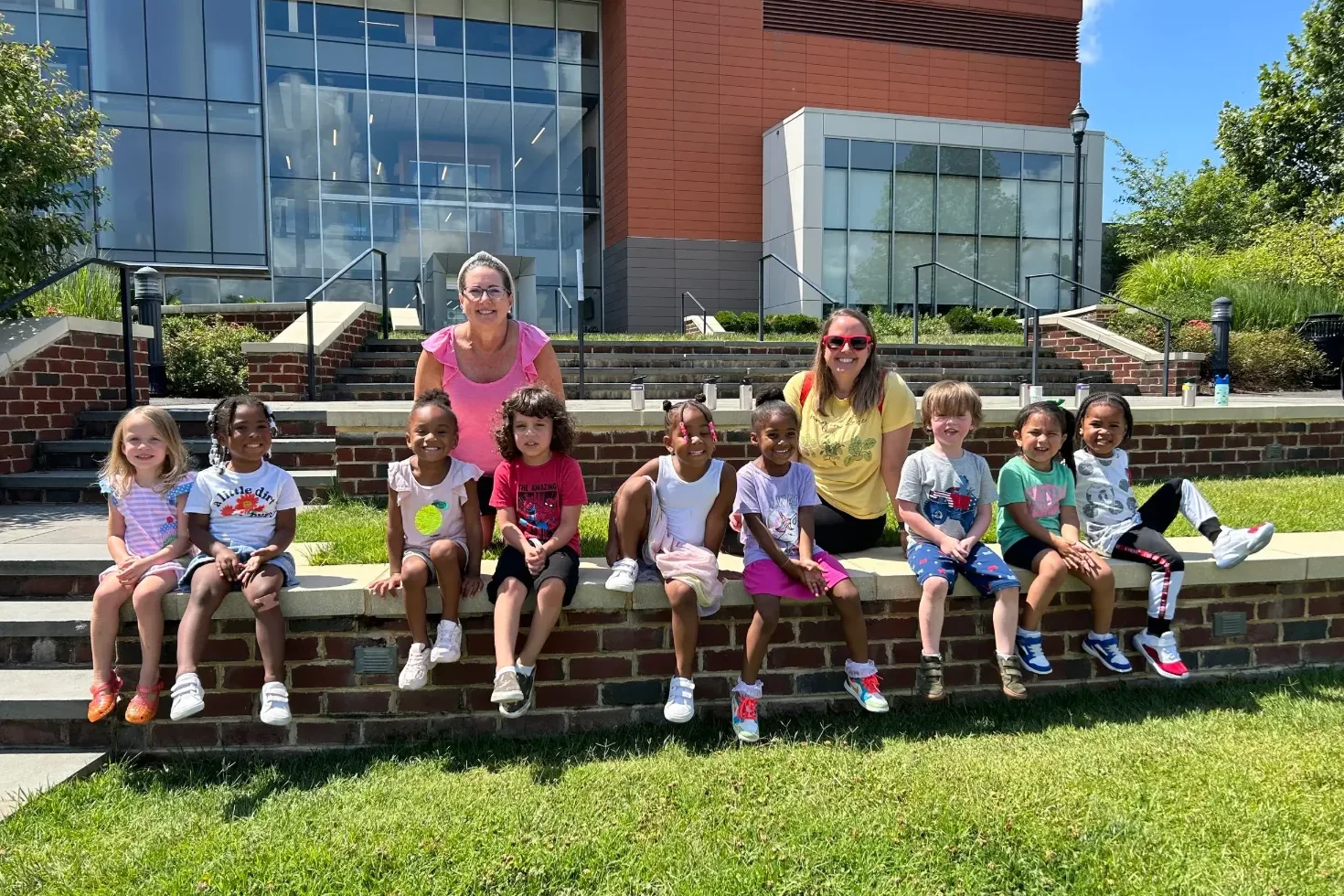 Children and teachers sitting together on a brick wall outside on a sunny day
